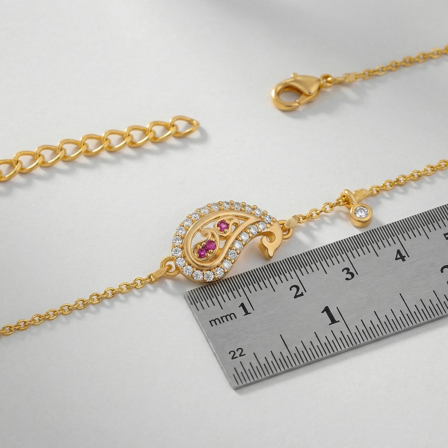 18k Gold plated bracelet with a decorative clasp and gemstones next to a ruler on a light gray background