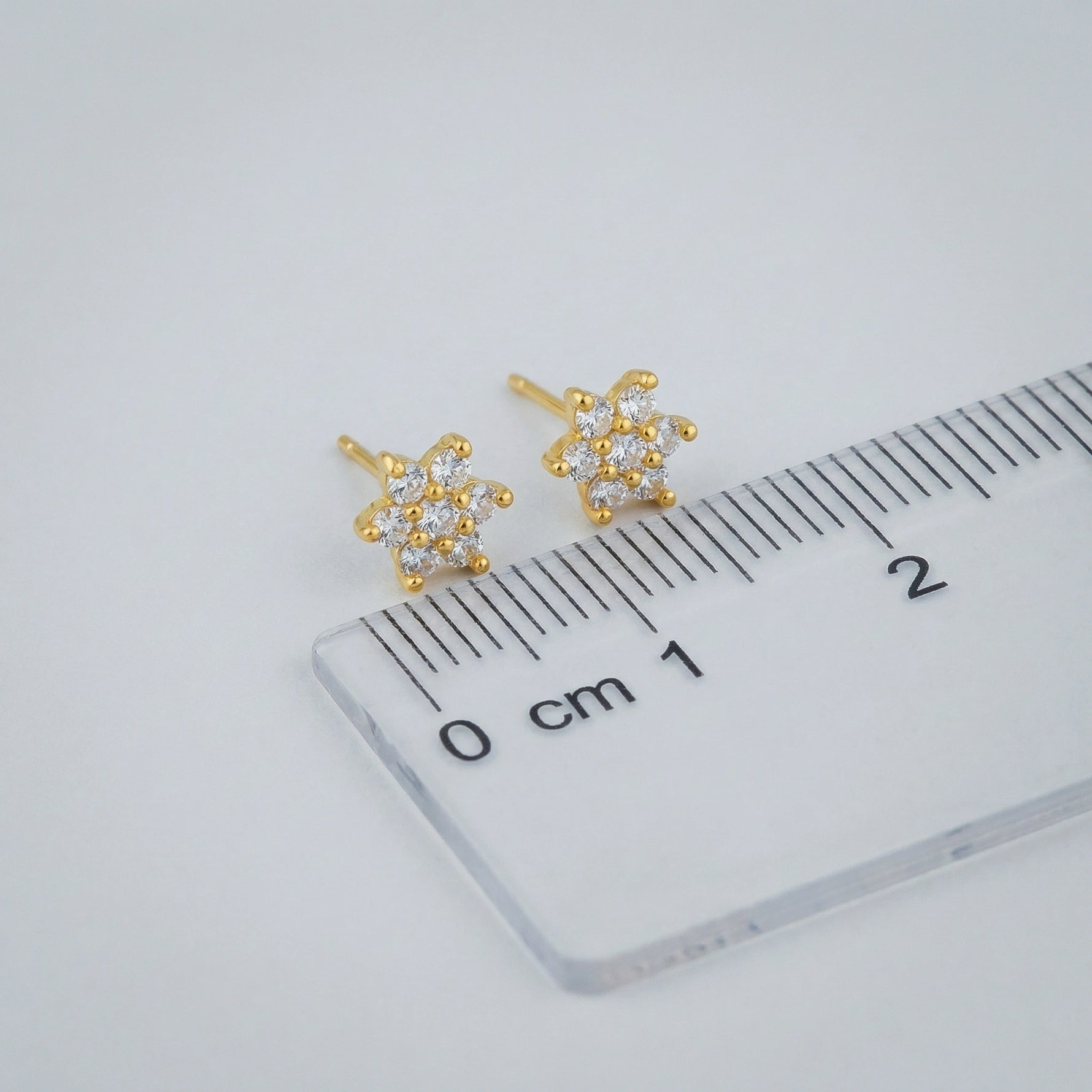 18k Gold plated arrings with clear stones on a ruler for scale, on a light gray background
