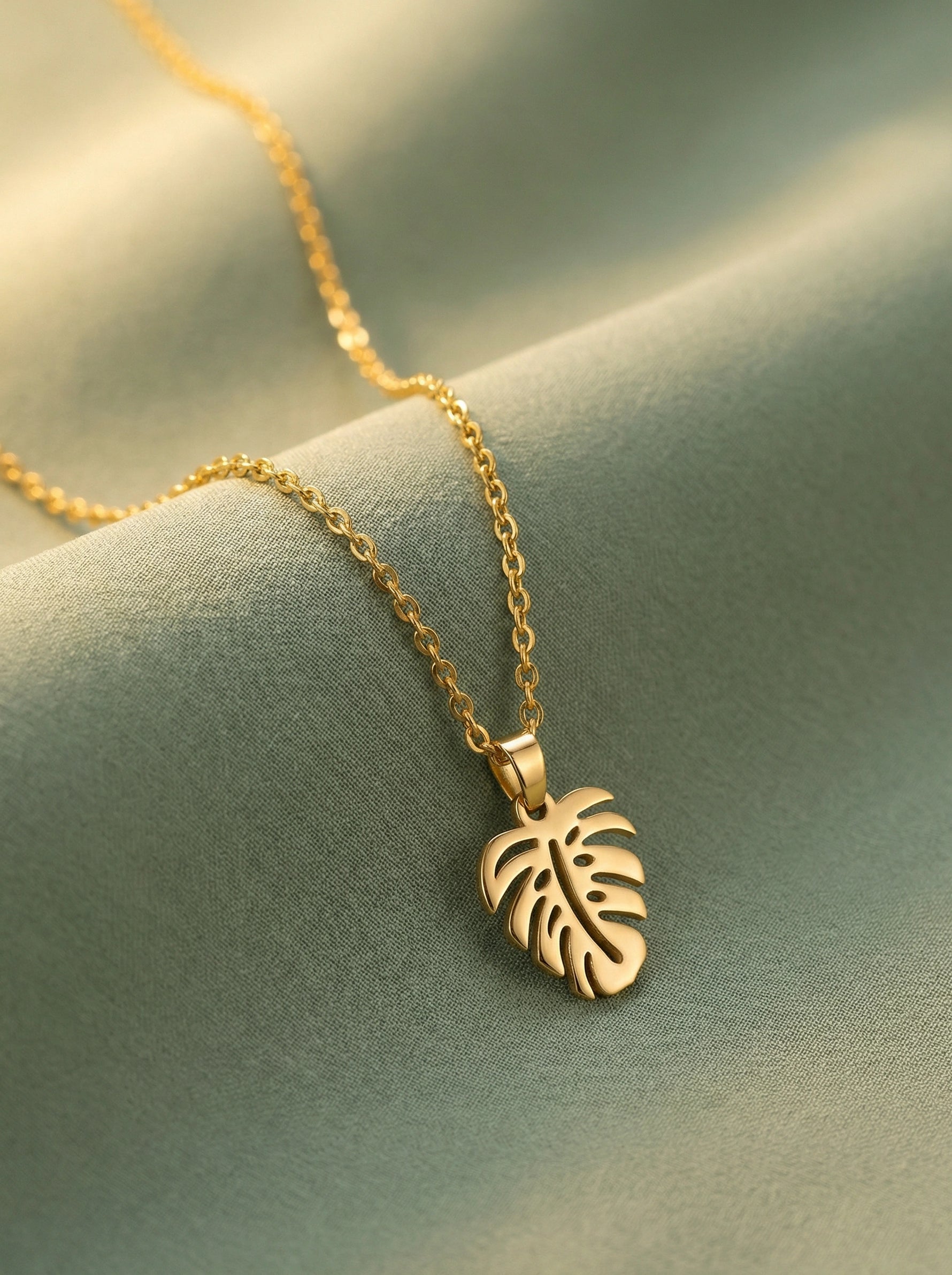 18k Gold plated necklace with a leaf pendant on a soft green fabric background