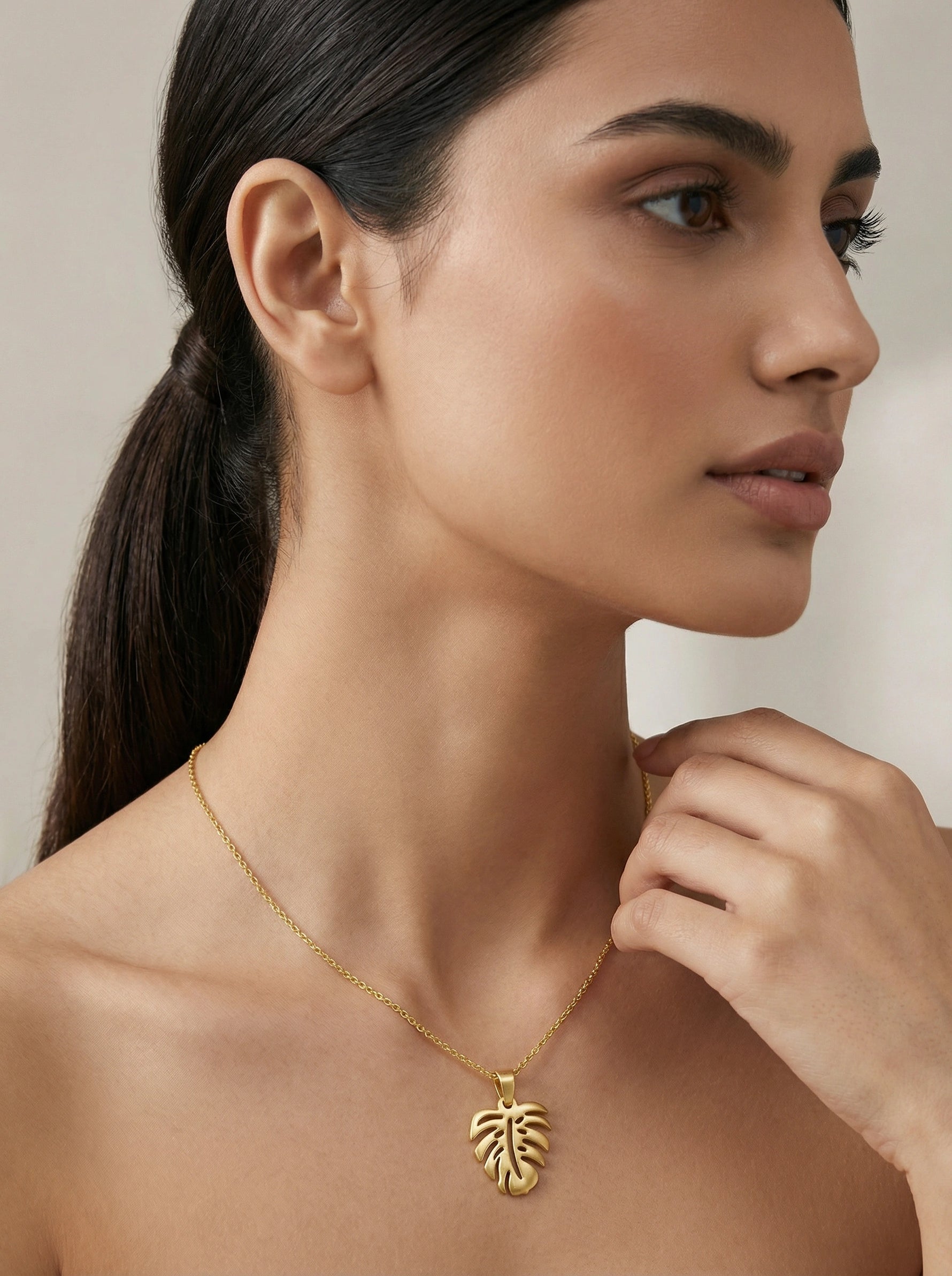 Woman wearing a 18k gold plated necklace with a leaf pendant against a neutral background