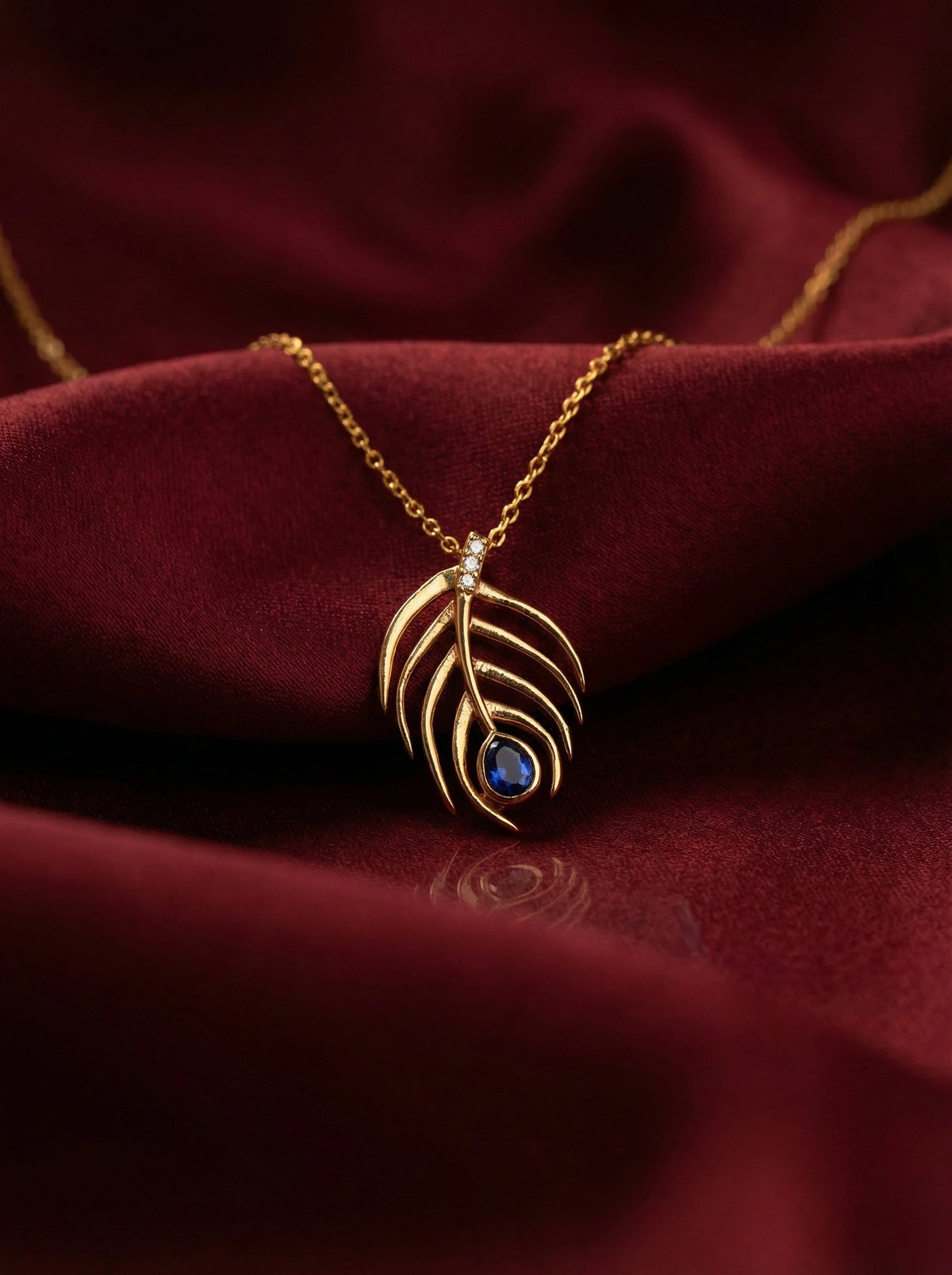18k Gold plated necklace with a leaf-shaped pendant featuring a blue gemstone on a red fabric background