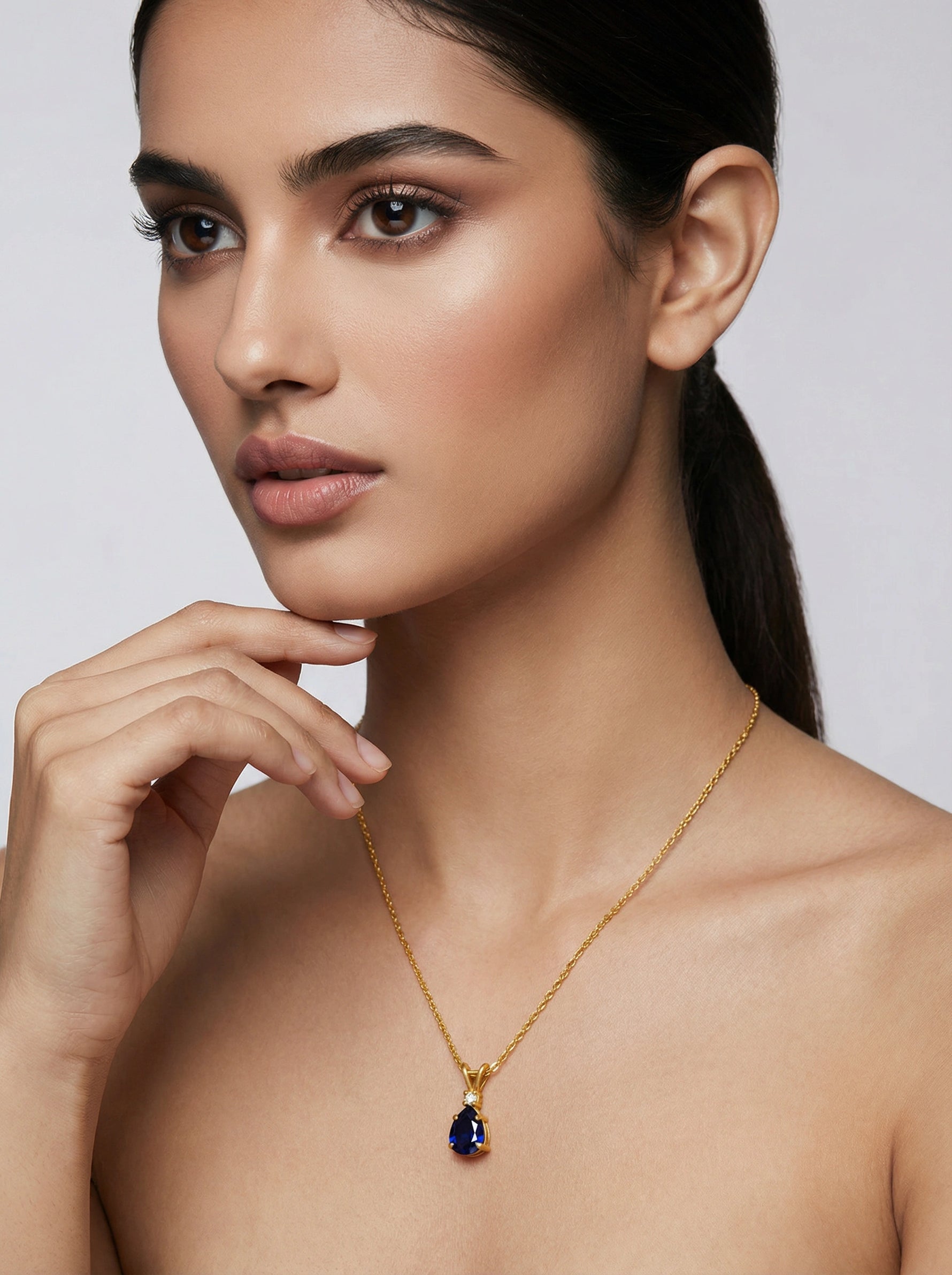 Woman wearing a 18k gold plated necklace with a blue pendant against a plain background