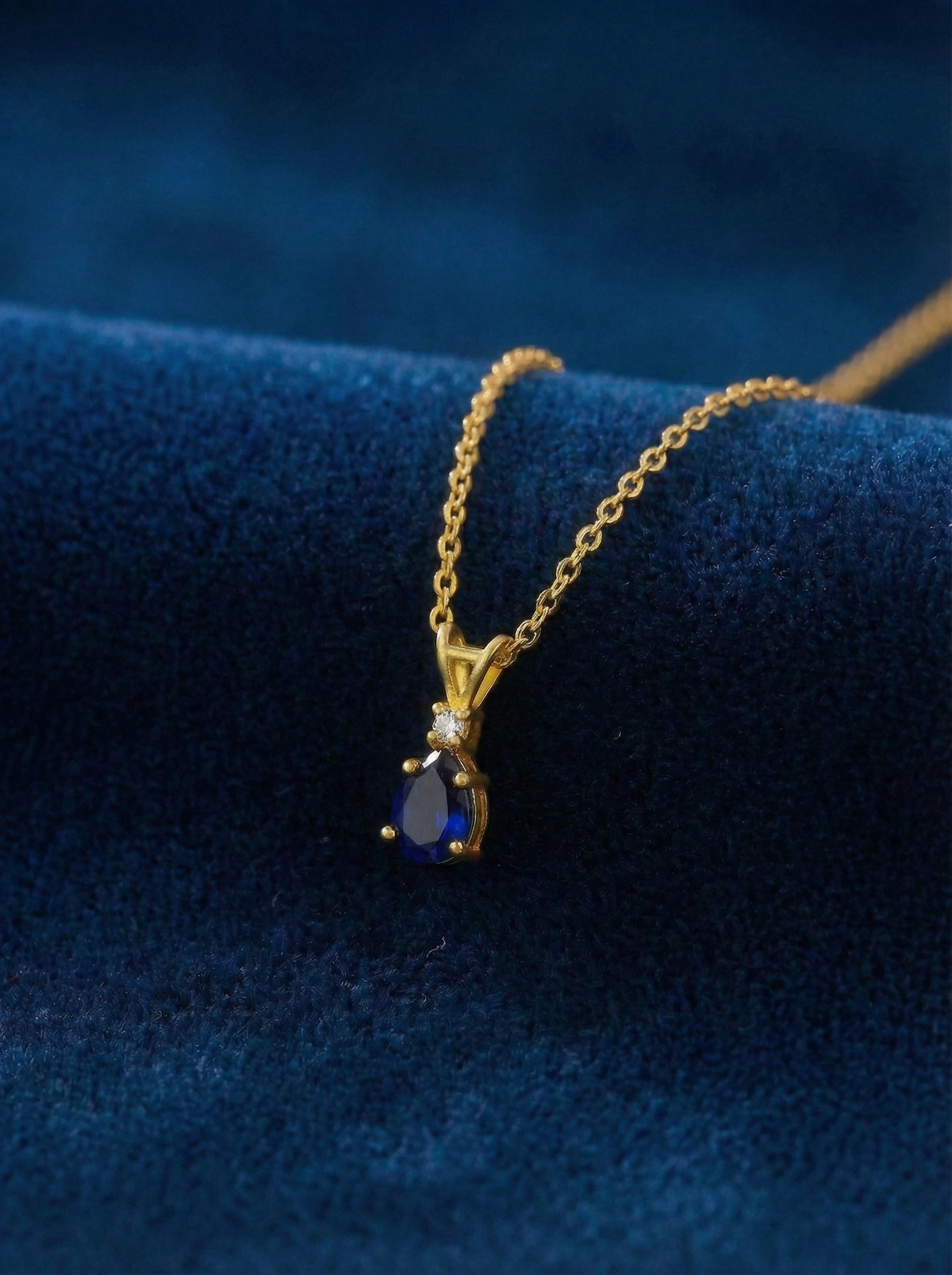 18k Gold plated necklace with a blue gemstone pendant on a blue fabric background