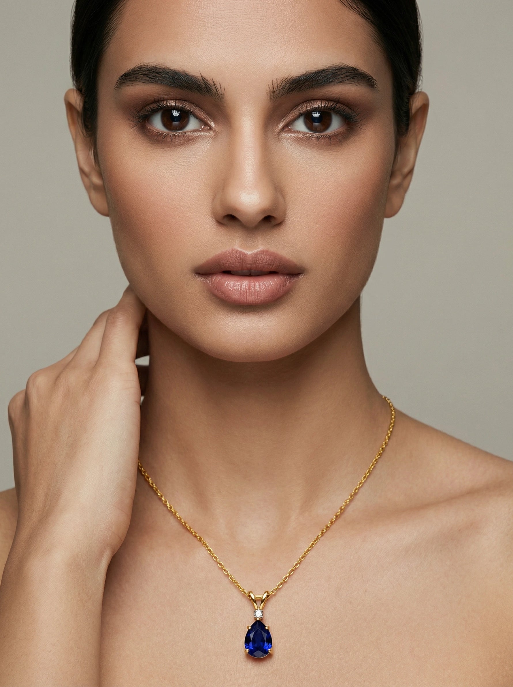 Woman wearing a 18k gold plated necklace with a blue pendant against a neutral background