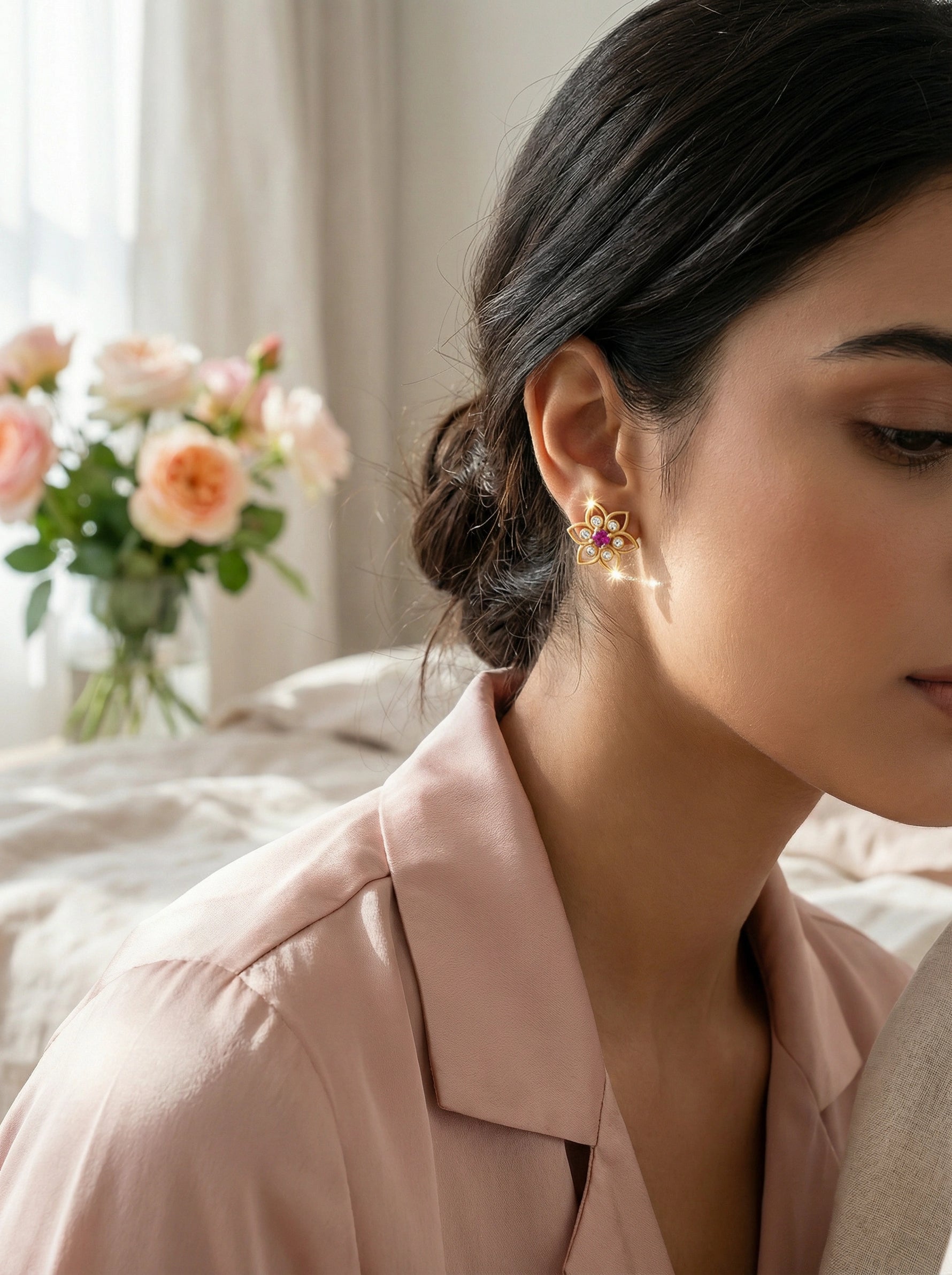Woman wearing 18k gold plated earrings with a blurred background of flowers and light curtains