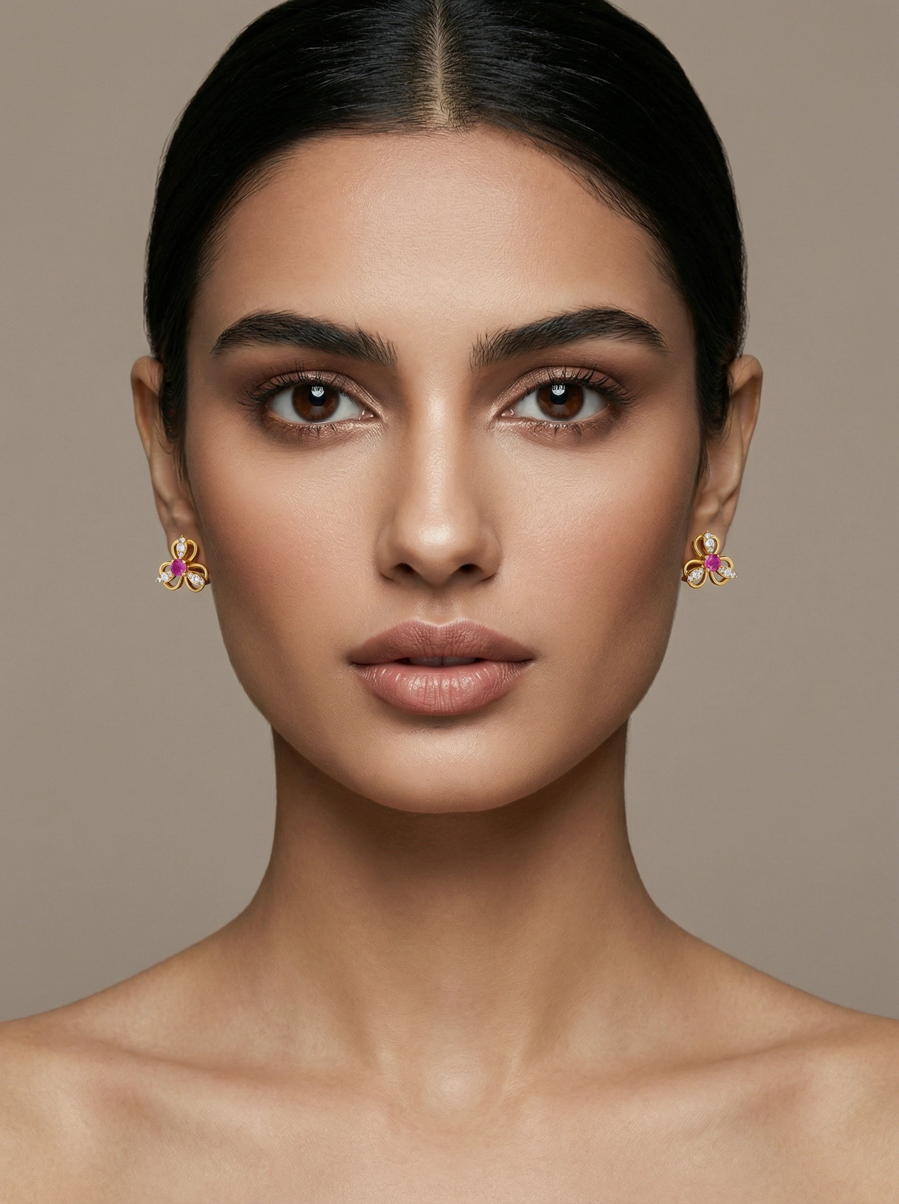 Close-up of a woman wearing 18k gold plated earrings with pink stones against a beige background