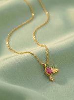 18k Gold plated necklace with a bird-shaped pendant featuring a pink gemstone on a light green fabric background