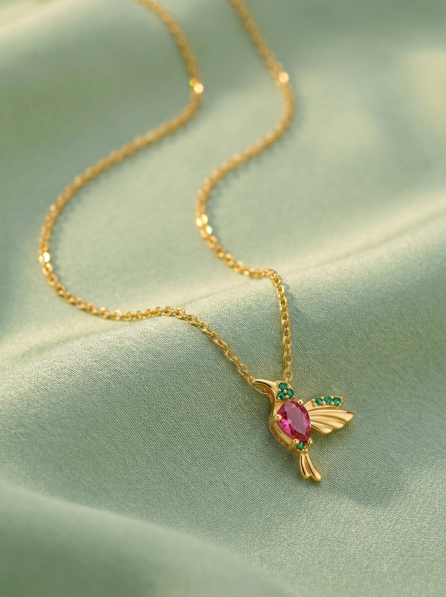 18k Gold plated necklace with a bird-shaped pendant featuring a pink gemstone on a light green fabric background