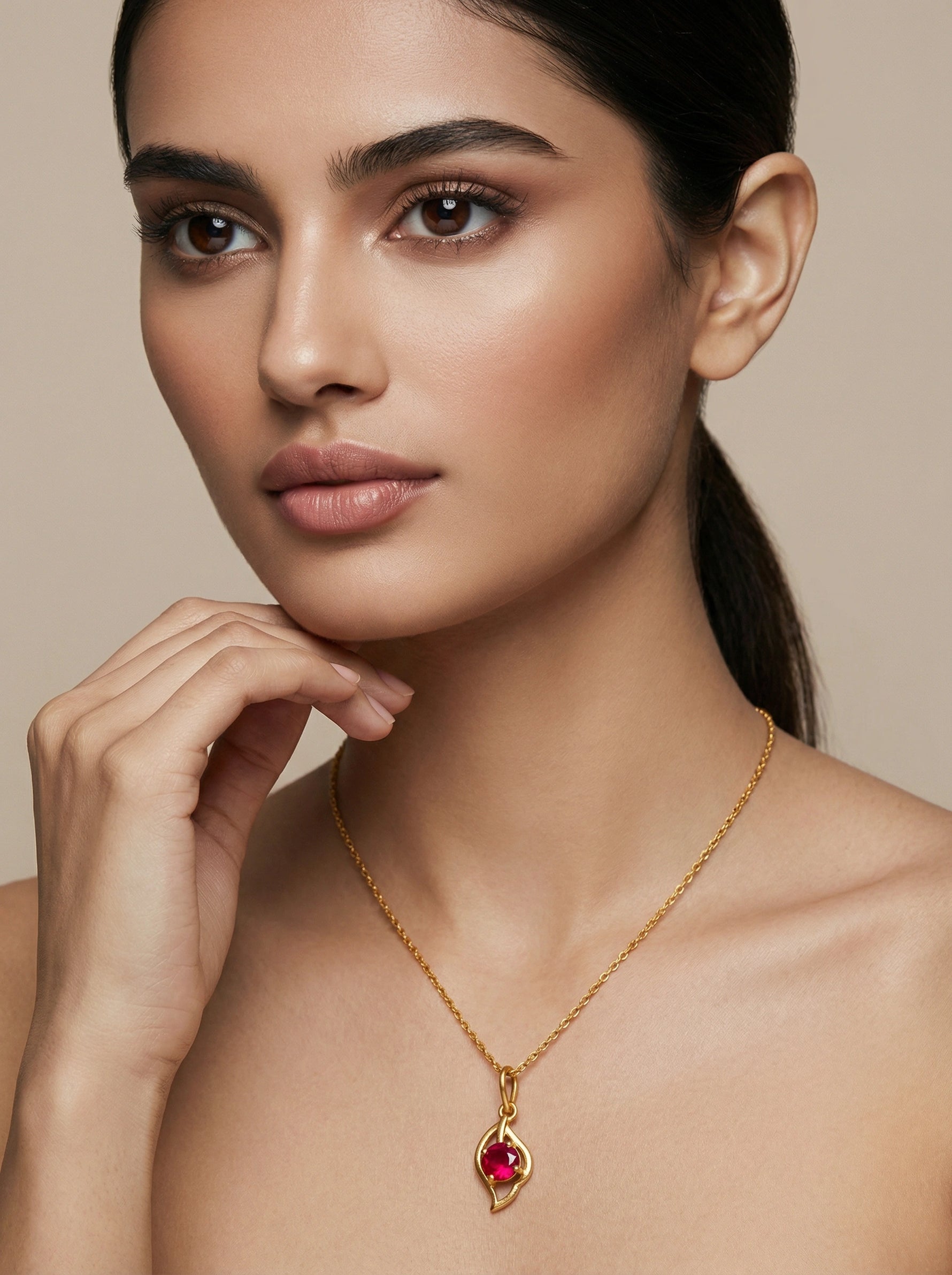 Woman wearing a 18k gold plated necklace with a red gemstone on a beige background
