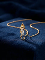 18k Gold plated seahorse necklace with diamonds on a blue fabric background
