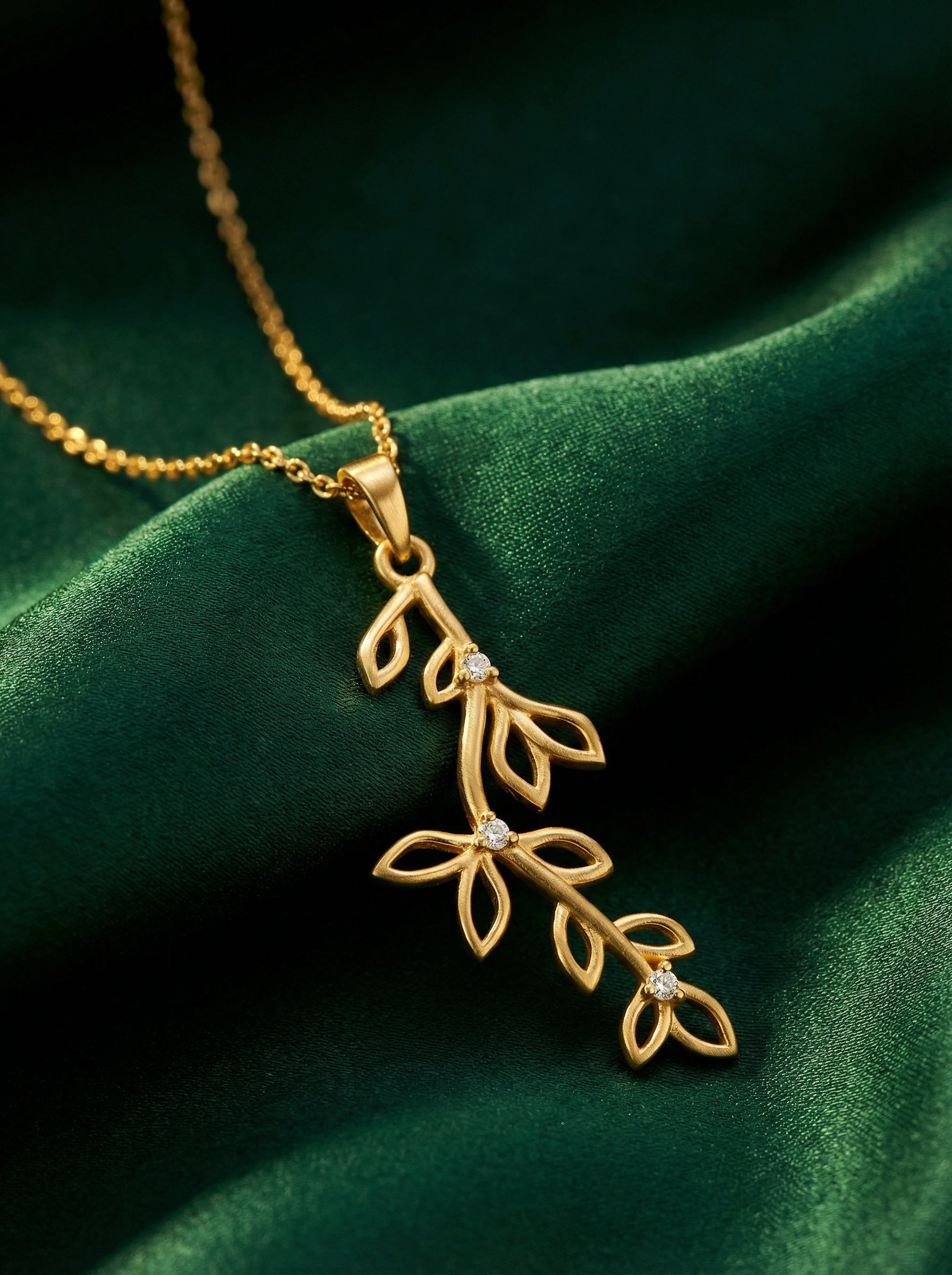 18k Gold plated necklace with leaf design pendant on a green fabric background