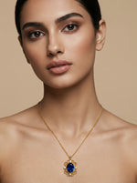 Woman wearing a 18k  gold plated  necklace with a blue gemstone pendant against a beige background