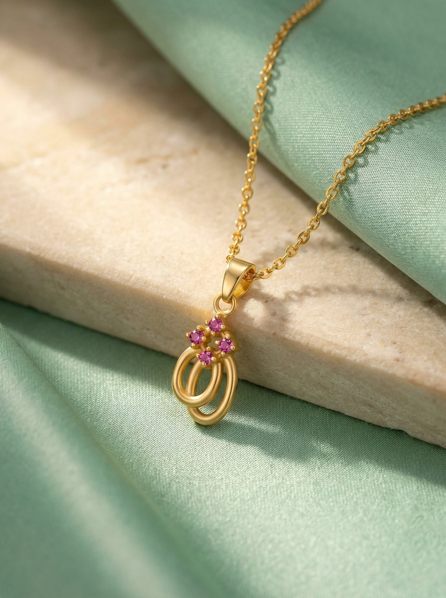 18k Gold plated necklace with a pendant featuring pink gemstones on a light green fabric background