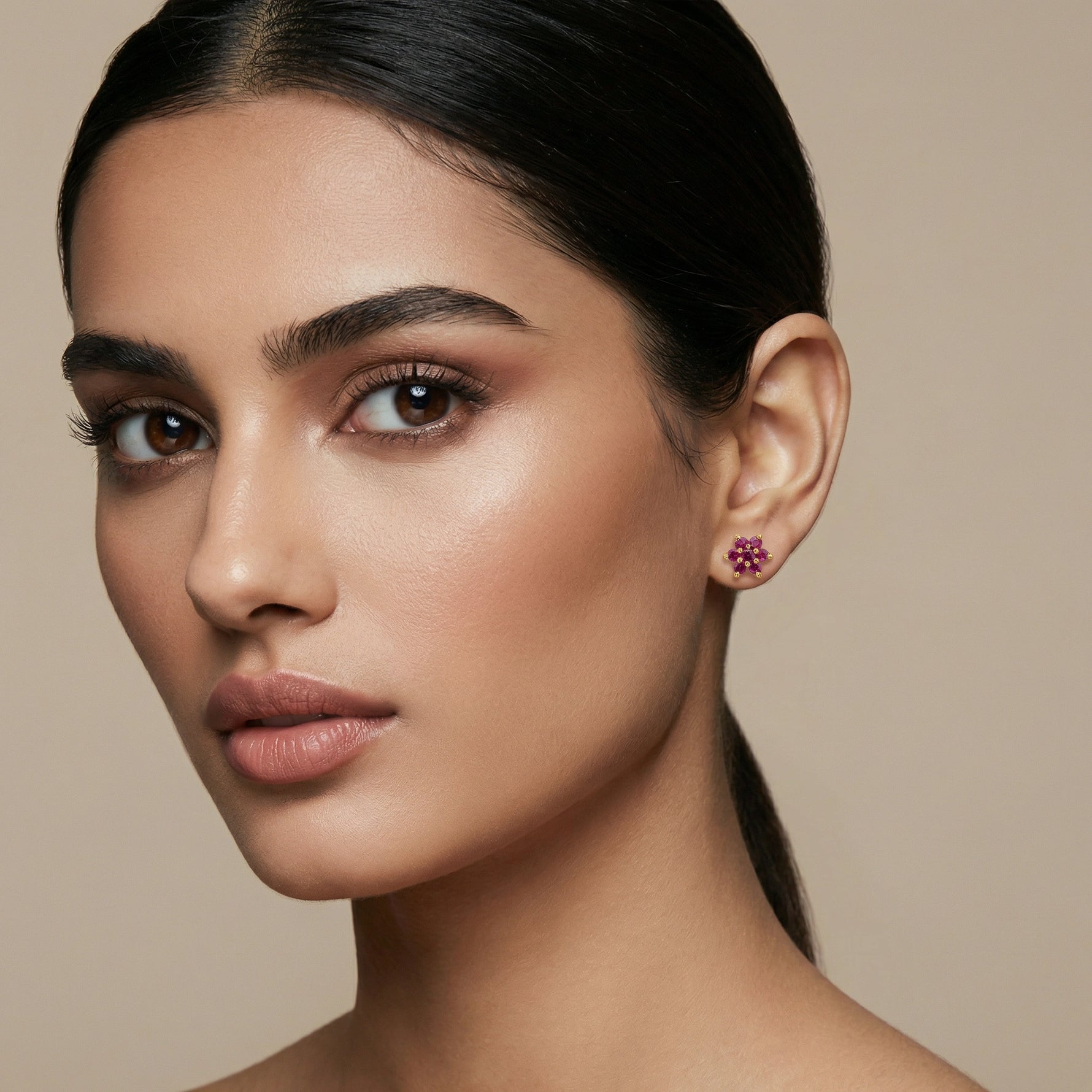 Close-up of a woman wearing a floral 18k gold plated earring against a beige background