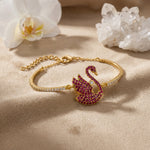 18k Gold plated bracelet with a swan charm on a beige surface with flowers and crystals.