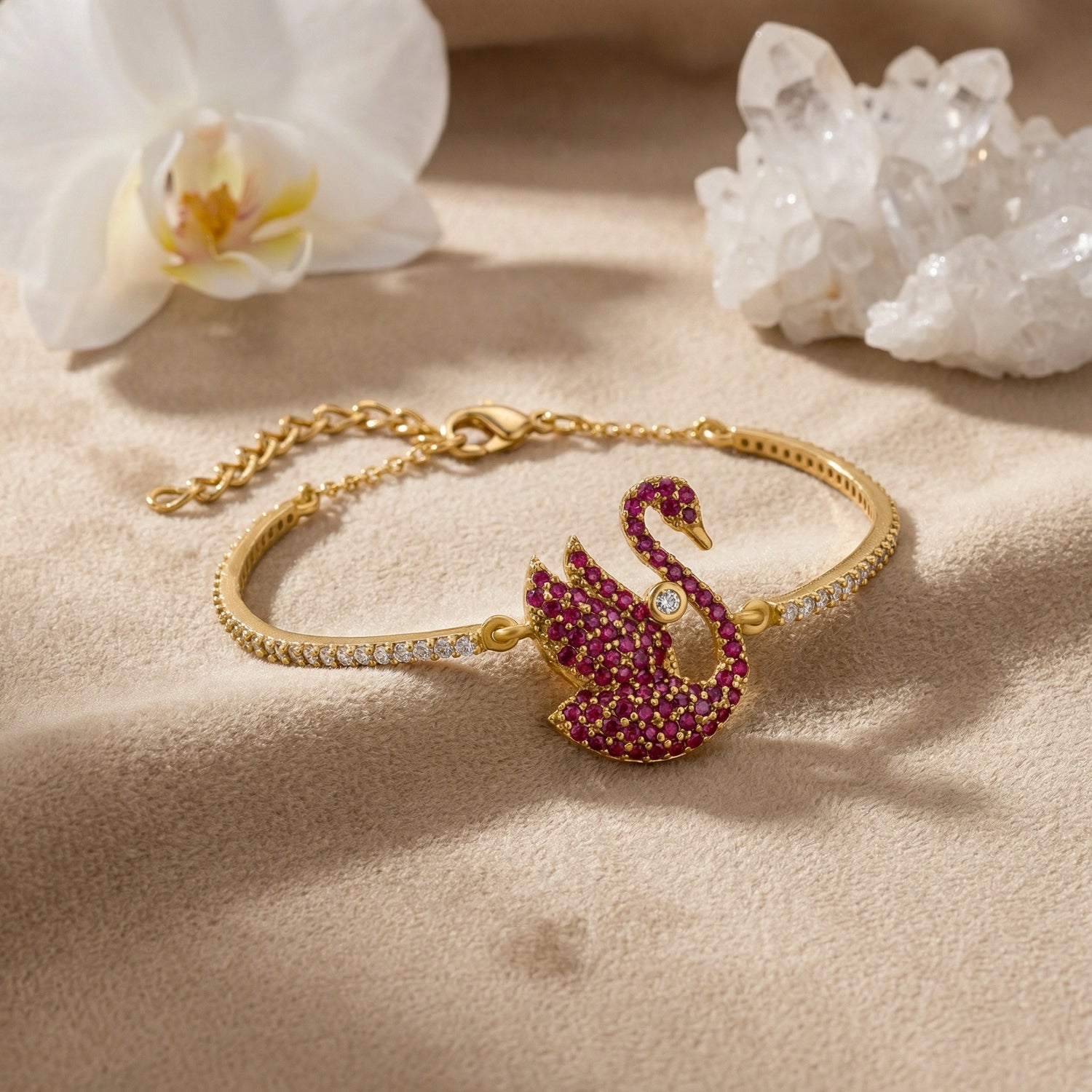 18k Gold plated bracelet with a swan charm on a beige surface with flowers and crystals.