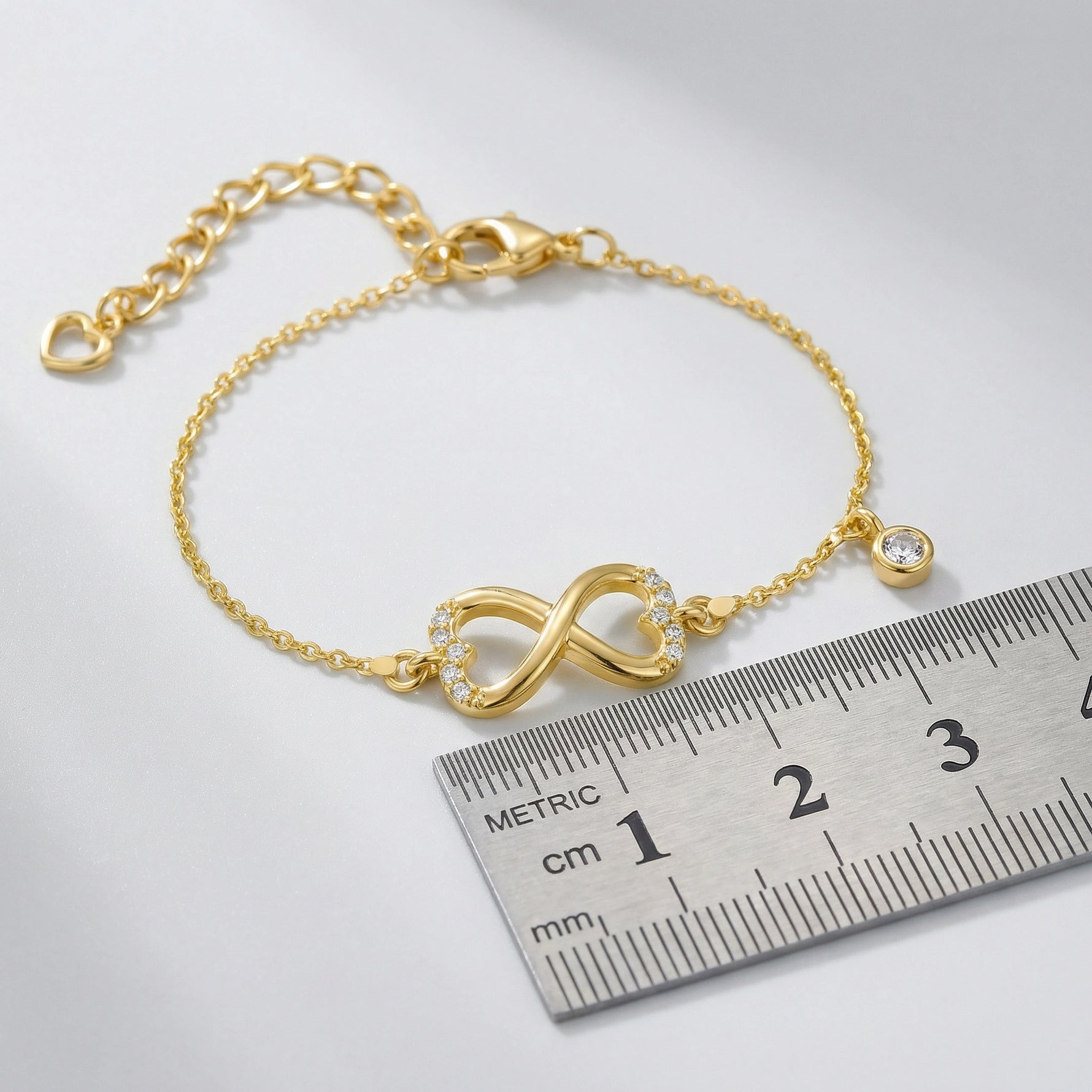 18k Gold plated bracelet with an infinity symbol next to a ruler on a white background