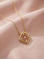 18k Gold plated necklace with a square pendant featuring red and clear stones on a pink fabric background