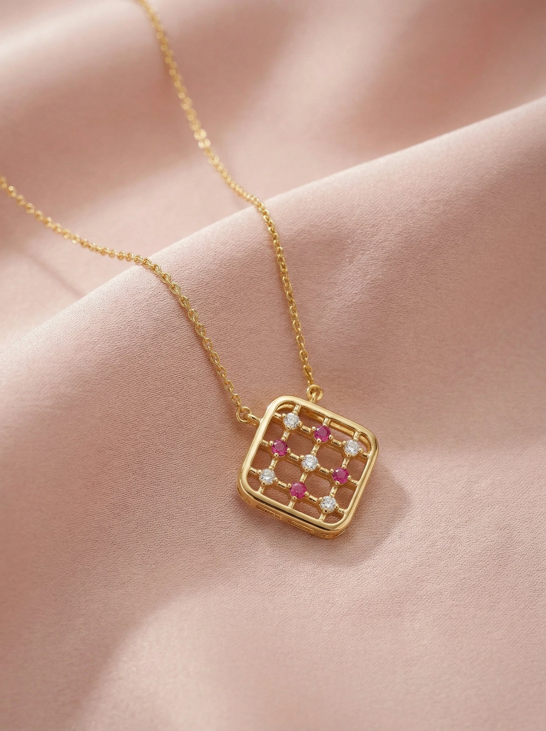 18k Gold plated necklace with a square pendant featuring red and clear stones on a pink fabric background