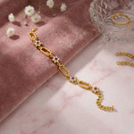 18k Gold plated  bracelet with gemstones on a pink marble surface with flowers and a glass dish.