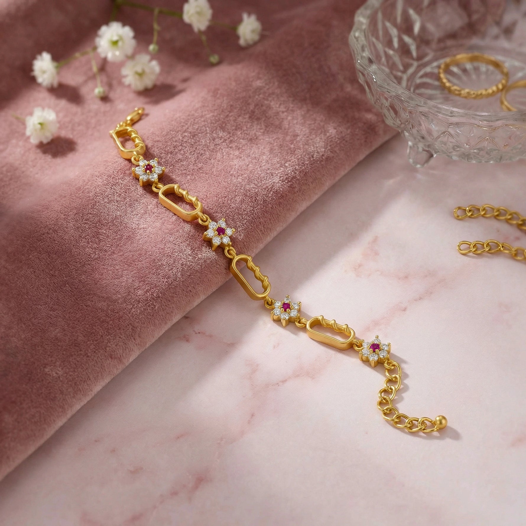 18k Gold plated  bracelet with gemstones on a pink marble surface with flowers and a glass dish.