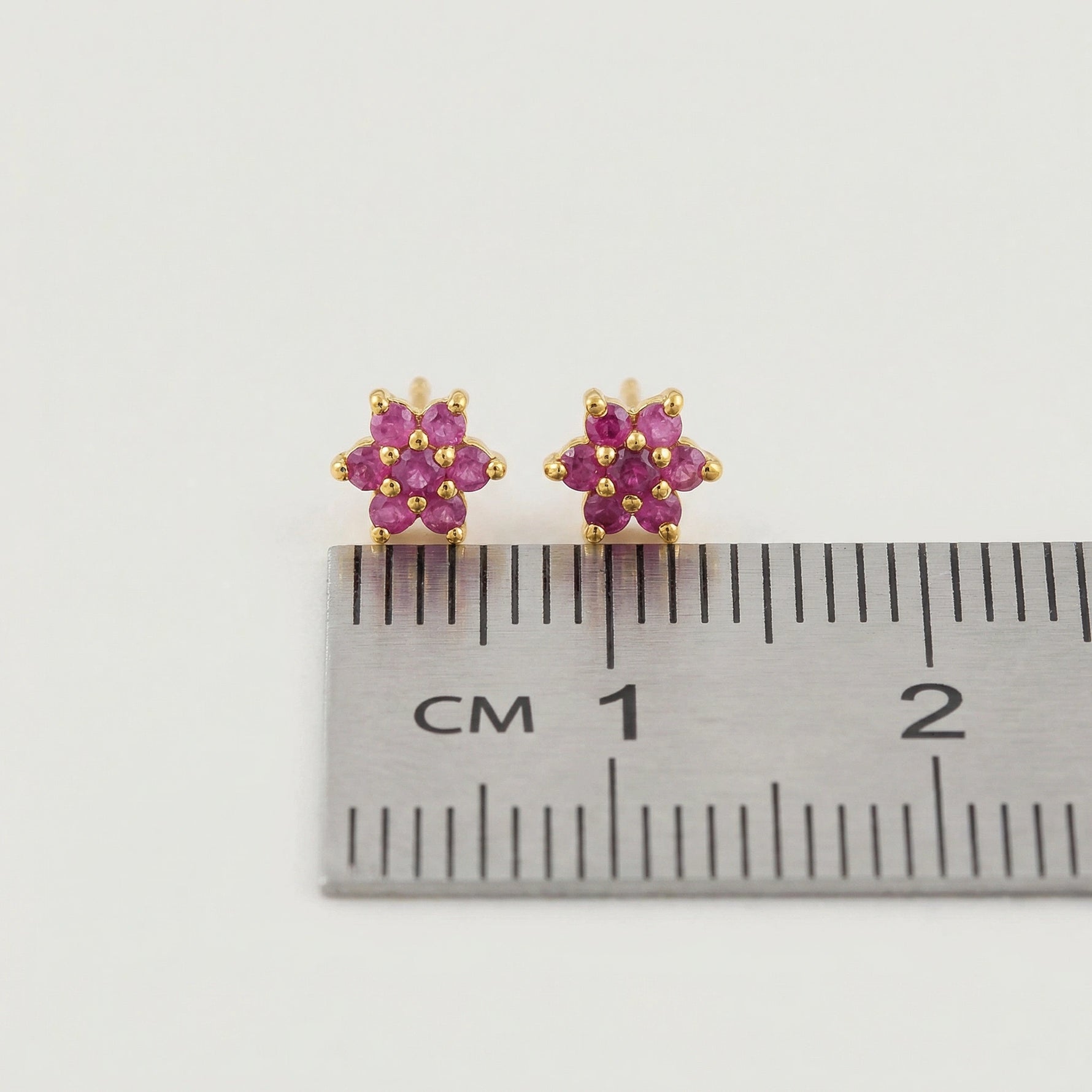 18k Gold plated earrings with pink gemstones next to a ruler for size reference on a white background