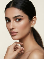 Woman with a smooth neck and ear, wearing 18k gold plated earrings against a beige background