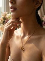 Woman wearing a 18k gold plated  necklace with a heart pendant, with a blurred floral background