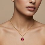 Close-up of a person wearing a 18k gold plated necklace with a red gemstone pendant on a beige background
