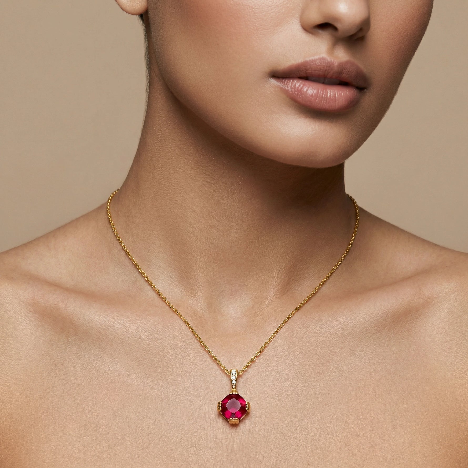 Close-up of a person wearing a 18k gold plated necklace with a red gemstone pendant on a beige background