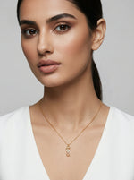 Woman wearing a 18k gold plated necklace with a unique pendant against a neutral background