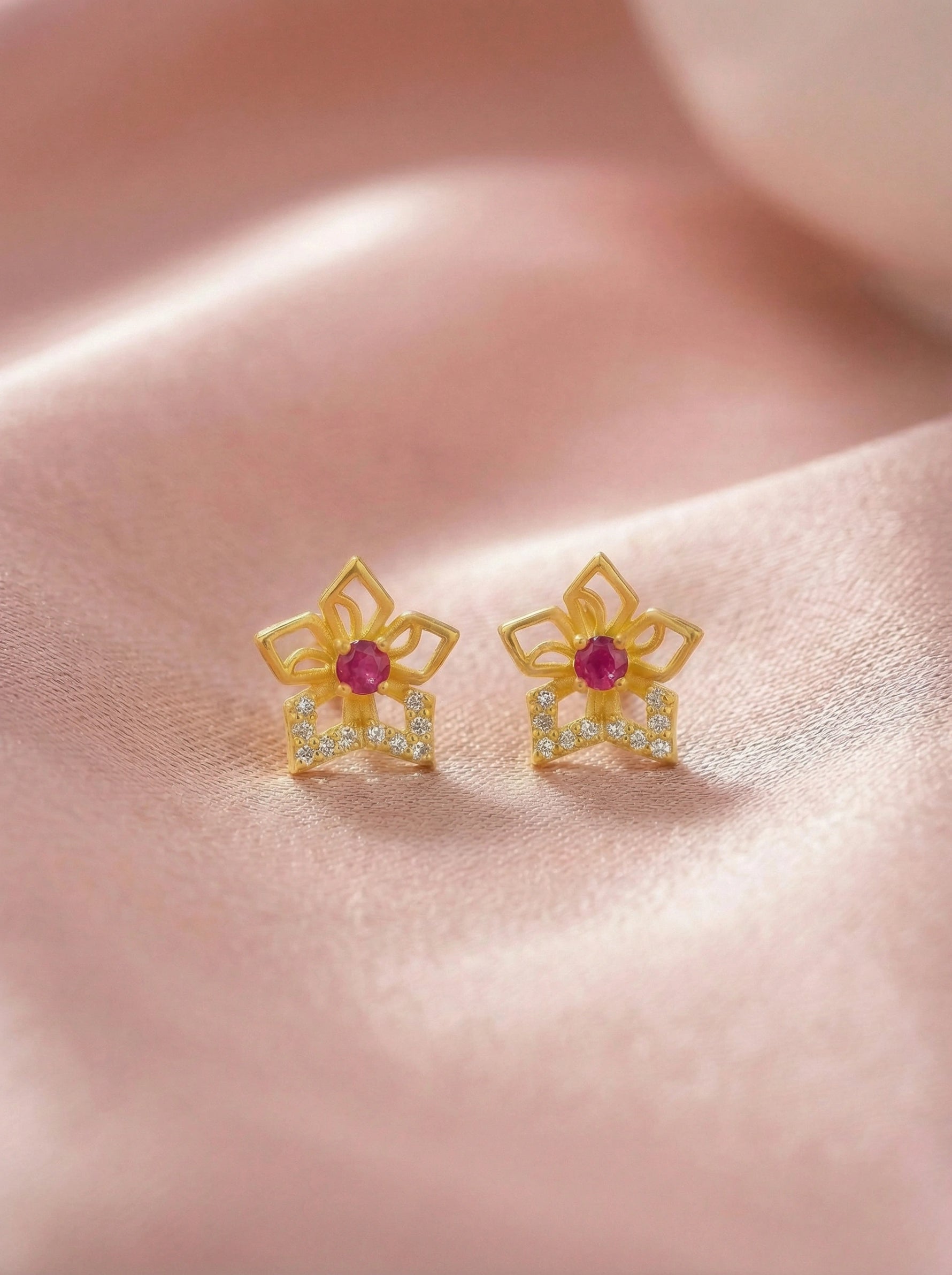 18k Gold plated earrings with red gemstones on a pink fabric background
