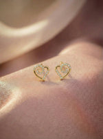 Heart-shaped 18k gold plated earrings on a soft pink fabric background