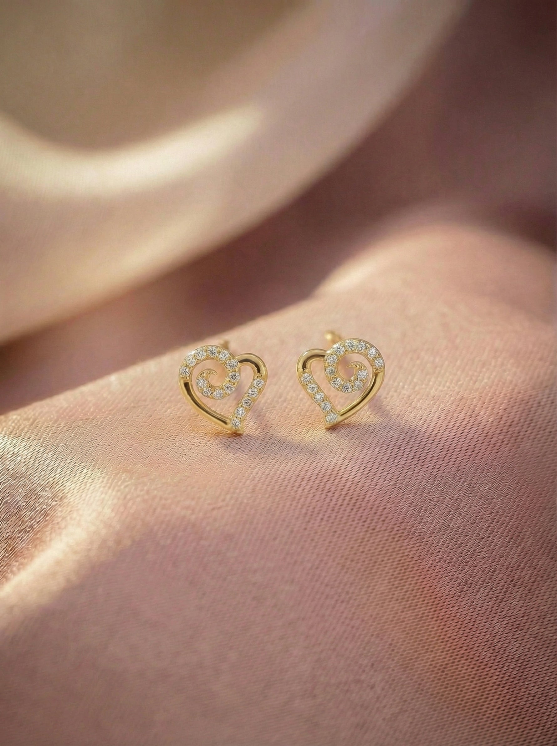 Heart-shaped 18k gold plated earrings on a soft pink fabric background