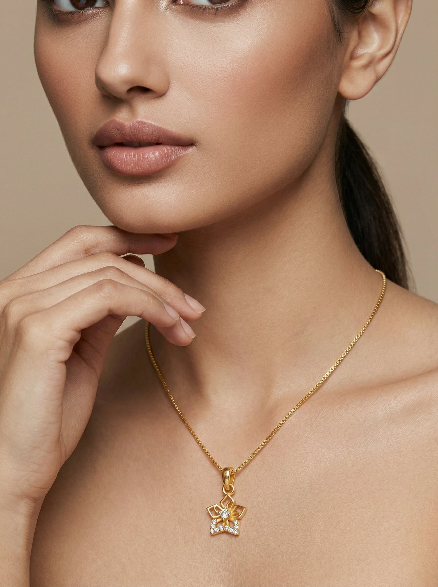Close-up of a woman wearing a 18k gold plated necklace with a star-shaped pendant on a beige background