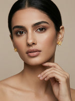Woman wearing 18k gold plated earrings against a beige background