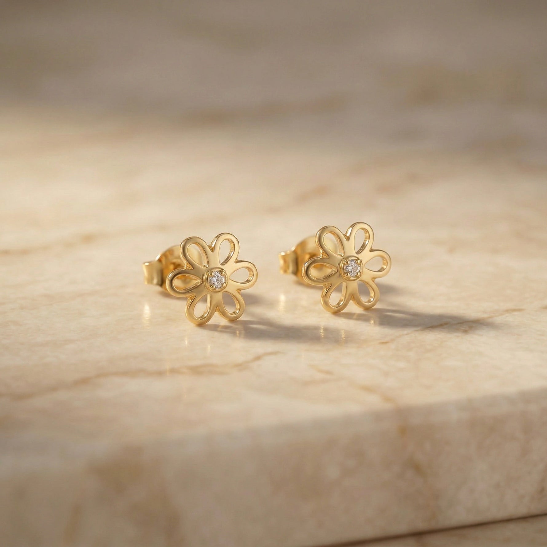 18k Gold plated flower-shaped earrings with diamonds on a beige marble surface