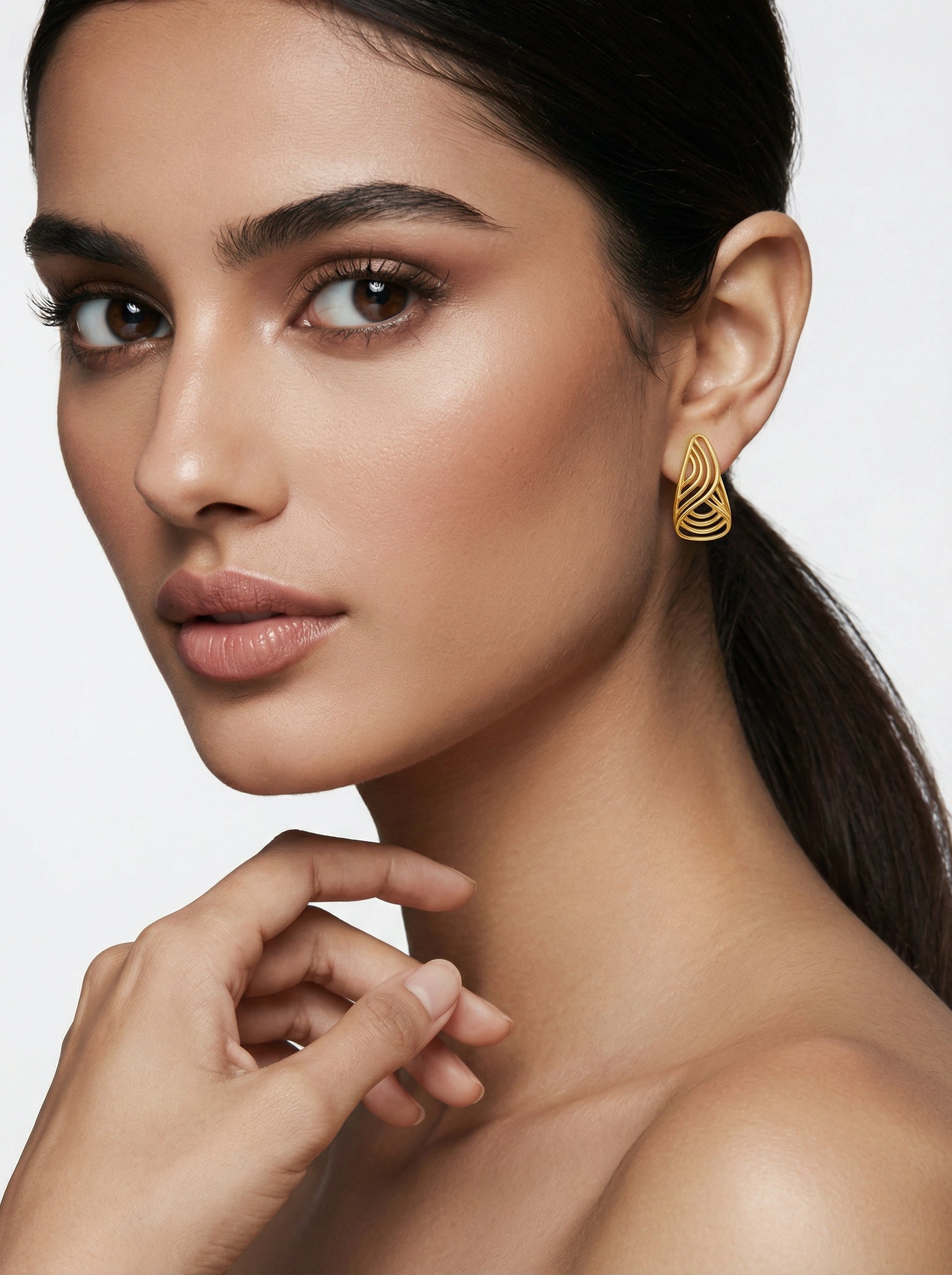 Close-up of a woman wearing 18k gold plated earrings with a neutral background