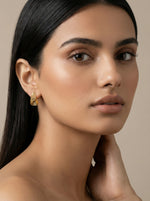 Woman wearing a 18k  gold plated earring against a neutral background
