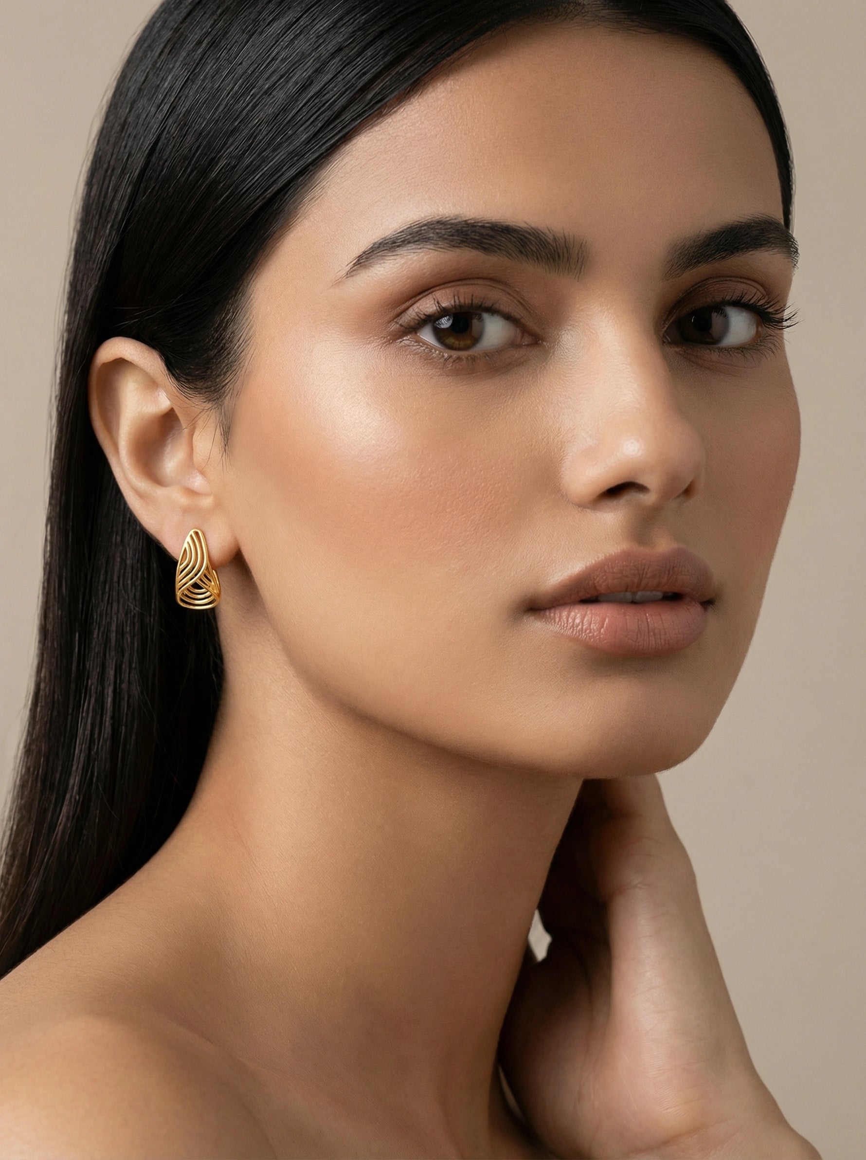 Woman wearing a 18k  gold plated earring against a neutral background